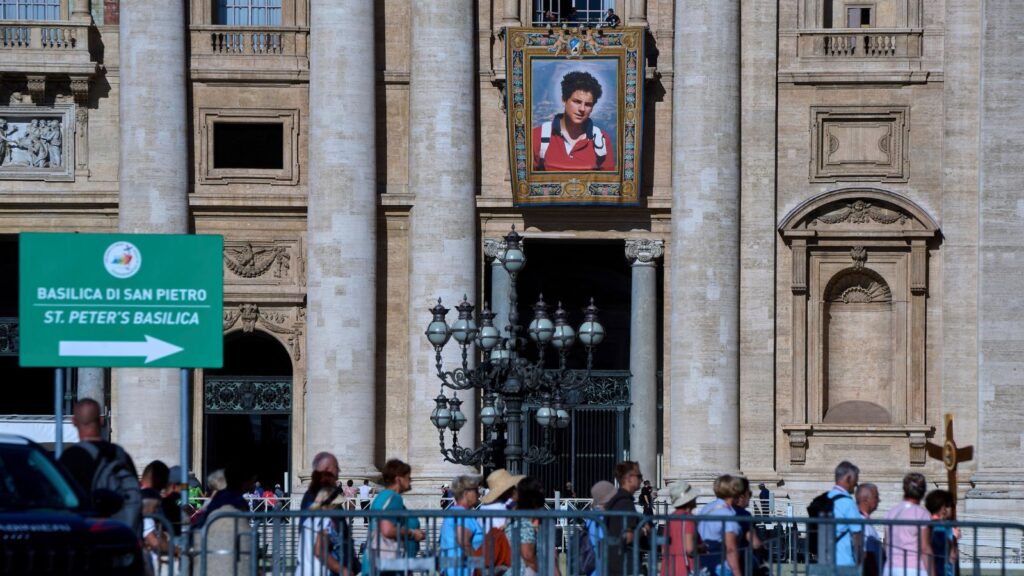 A tapestry with a portrait of Blessed Carlo Acutis, who will be canonized on Sunday, hangs on the facade of St. Peter's Basilica at the Vatican, Thursday, Sept. 4, 2025, as Jubilee pilgrims arrive to walk through the Holy Door. (AP Photo/Domenico Stinellis) Sainthood