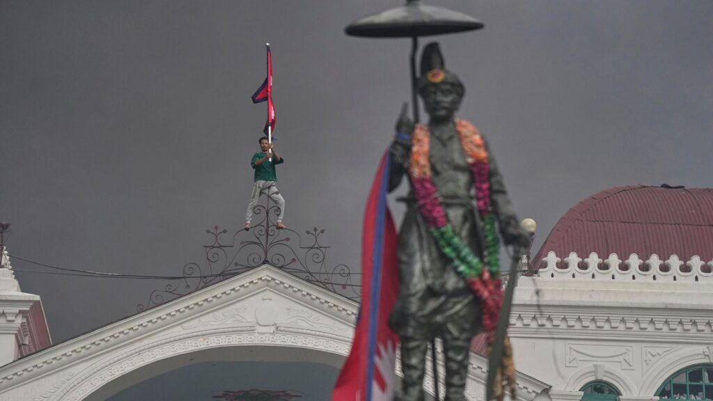 A protester celebrates standing at the top of the Singha Durbar, the seat of Nepal's government's various ministries and offices, after it was set on fire during a protest against social media ban and corruption in Kathmandu, Nepal, Tuesday, Sept. 9, 2025. (AP Photo/Niranjan Shrestha)